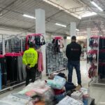 Ves una persona de la Policía y una persona del CTI.  Al fondo se puede ver la mercancía textil incautada.