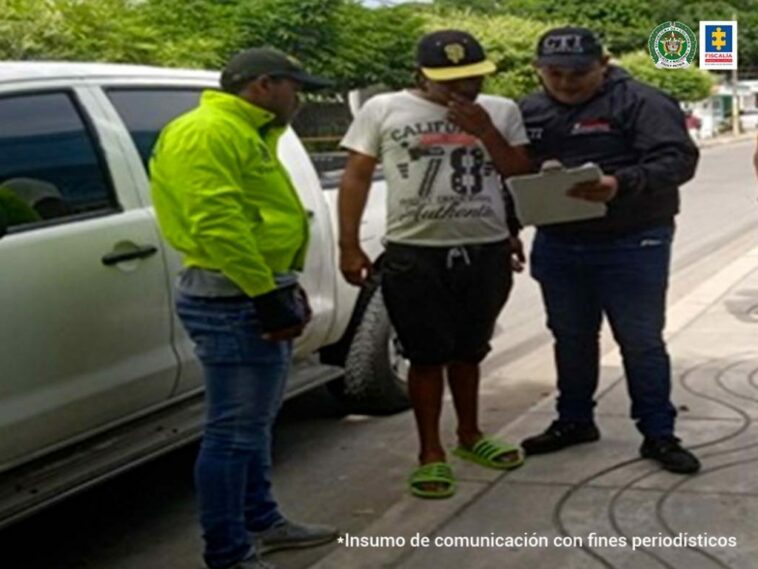 En la imagen se ve a una persona quien va a ser capturada por un policía y un funcionario del CTI, junto a una camioneta.