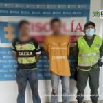 En la fotografía aparecen dos hombres capturados, junto a personal de la Policía Nacional. En la parte posterior de la imagen se ve un banner de la Fiscalía con texto alternativo.