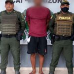 En la foto observamos a un hombre con camiseta roja y bermuda negra, custodiado por dos agentes de la Policía Nacional en un CAI .