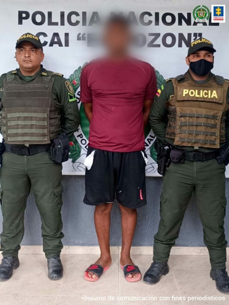 En la foto observamos a un hombre con camiseta roja y bermuda negra, custodiado por dos agentes de la Policía Nacional en un CAI .