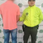 En la foto está el detenido de espaldas, custodiado por un uniformado de la Policía Nacional. Detrás un banner de esa institución.