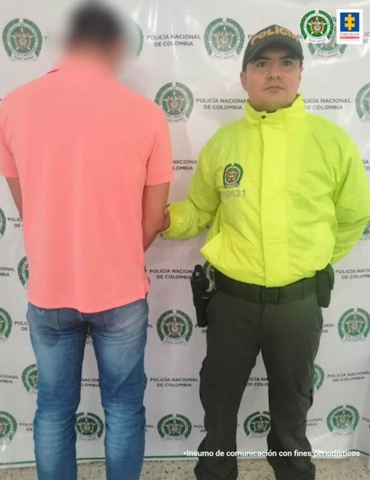 En la foto está el detenido de espaldas, custodiado por un uniformado de la Policía Nacional. Detrás un banner de esa institución.