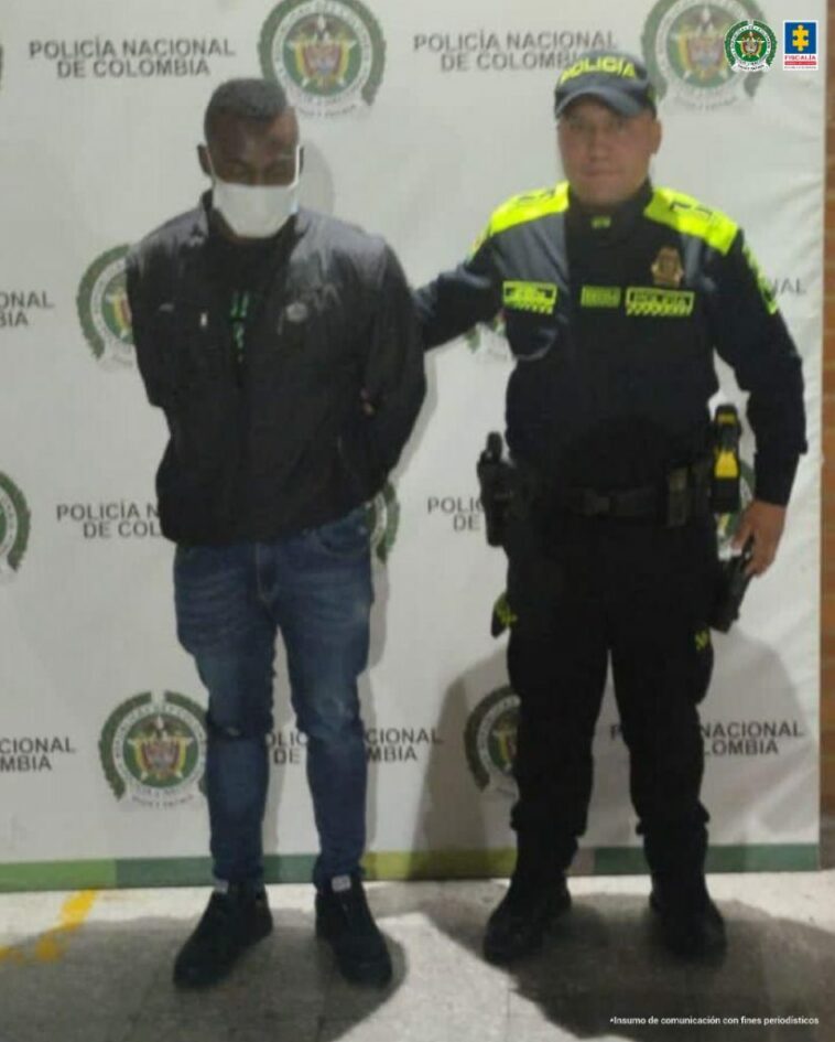 En la fotografía aparece un hombre capturado, junto a un agente de la Policía Nacional. En la parte posterior de la imagen se ve un banner de la Policía Nacional
