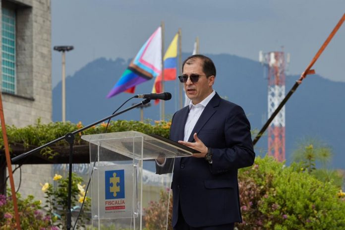 En la imagen el Fiscal General de la Nación, Francisco Barbosa Delgado aparece dando un discurso. Al fondo puede verse la bandera de la Fiscalía, la de Colombia y la de la población LGBTIQ+