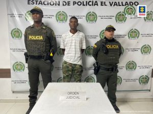 En la fotografía aparece un hombre capturado, junto a dos agentes de la Policía Nacional. En la parte posterior de la imagen se ve un banner de la Policía Nacional.