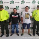 En la foto dos capturados con dos miembros de la Policía Nacional. Detrás suyo un backing de la misma institución.