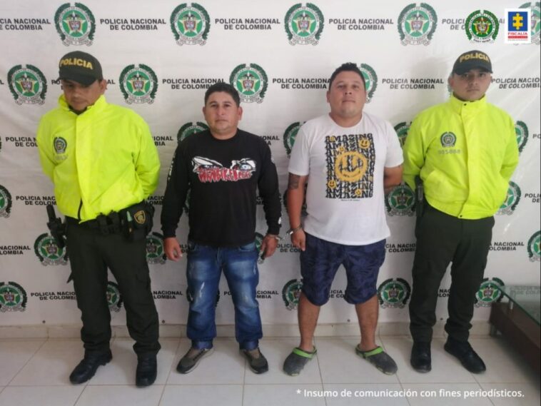 En la foto dos capturados con dos miembros de la Policía Nacional. Detrás suyo un backing de la misma institución.