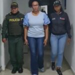 En la foto aparece Mavy Yineth Viera Angulo, ex alcaldesa de Buenaventura (Valle) vestida con un jean azul, una blusa de mangas cortas azul clara, cabello recogido y lentes. Al lado derecho de ella hay un uniformado de la Policía Nacional y a su izquierda una servidora del CTI.