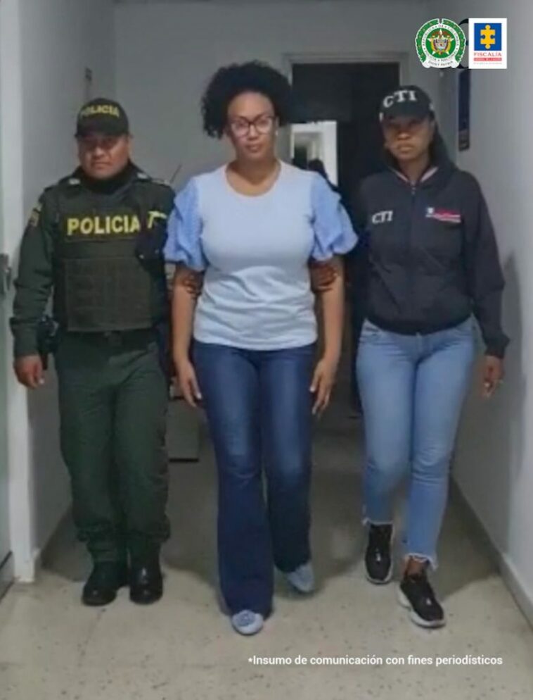 En la foto aparece Mavy Yineth Viera Angulo, ex alcaldesa de Buenaventura (Valle) vestida con un jean azul, una blusa de mangas cortas azul clara, cabello recogido y lentes. Al lado derecho de ella hay un uniformado de la Policía Nacional y a su izquierda una servidora del CTI.