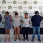 En la fotografía aparecen cuatro capturados, tres mujeres y un hombre, acompañados de uniformados   de la Policía Nacional. En la parte posterior un banner con logos de la Policía.