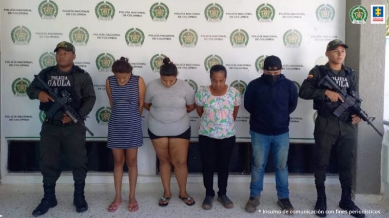 En la fotografía aparecen cuatro capturados, tres mujeres y un hombre, acompañados de uniformados   de la Policía Nacional. En la parte posterior un banner con logos de la Policía.