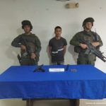 En la imagen se aprecia al capturado junto a dos uniformados de la Policía Nacional. Al frente en una mesa se observa la pistola y munición incautada.