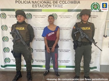 En la fotografía se observa al capturado junto a dos uniformados de la Policía Nacional. En la parte posterior se visualiza el banner que identifica a la Policía Nacional en Tame (Arauca)