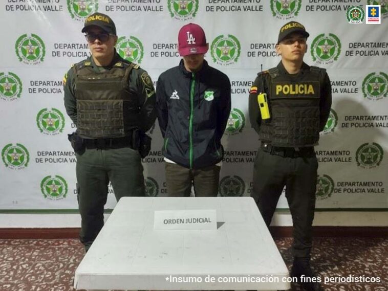 En la foto aparecen de pie y con los brazos atrás, José Ignacio Vélez Alzate. Viste con buzo oscuro con cierre verde y dos estampados a la altura del pecho; pantalón verde y gorra vinotinto. A lado y lado de él hay uniformados de la Policía Nacional. Delante de ellos hay una mesa blanca con un letrero que dice: ‘orden judicial’. Detrás de ellos hay un pendón institucional de la Policía.