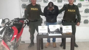 En la fotografía aparece el capturado junto a dos agentes de la Policía Nacional. En la parte posterior se observa una mesa con un arma de fuego, munición y dos teléfonos celulares.