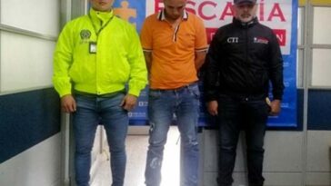 En la fotografía se observa al capturado junto a un investigador del CTI y un funcionario de la SIJIN. En la parte posterior se aprecia el banner que identifica a la Fiscalía General de la Nación