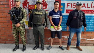 En la fotografía aparece un capturado, junto a personal de Ejército Nacional, Policía Nacional y  Fiscalía General de la Nación. En la parte posterior de la imagen se ven banners de Ejército Nacional, Policía Nacional y la Fiscalía General de la Nación.