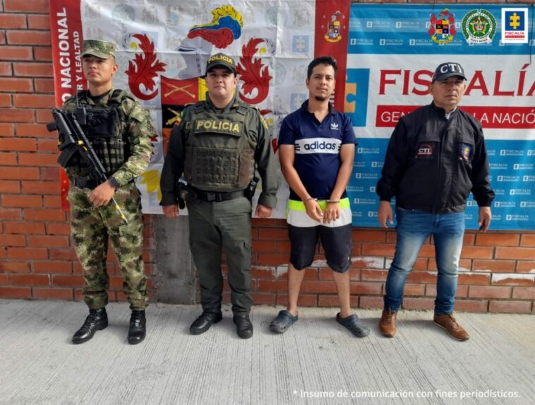 En la fotografía aparece un capturado, junto a personal de Ejército Nacional, Policía Nacional y  Fiscalía General de la Nación. En la parte posterior de la imagen se ven banners de Ejército Nacional, Policía Nacional y la Fiscalía General de la Nación.