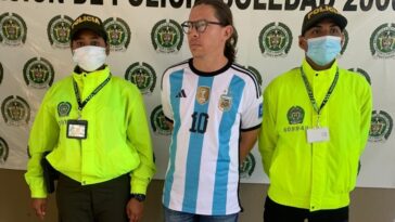 El capturado aparece en el centro de la imagen, con una camiseta de equipo deportivo y gafas. A cada lado tiene a personal de la Policía Nacional.