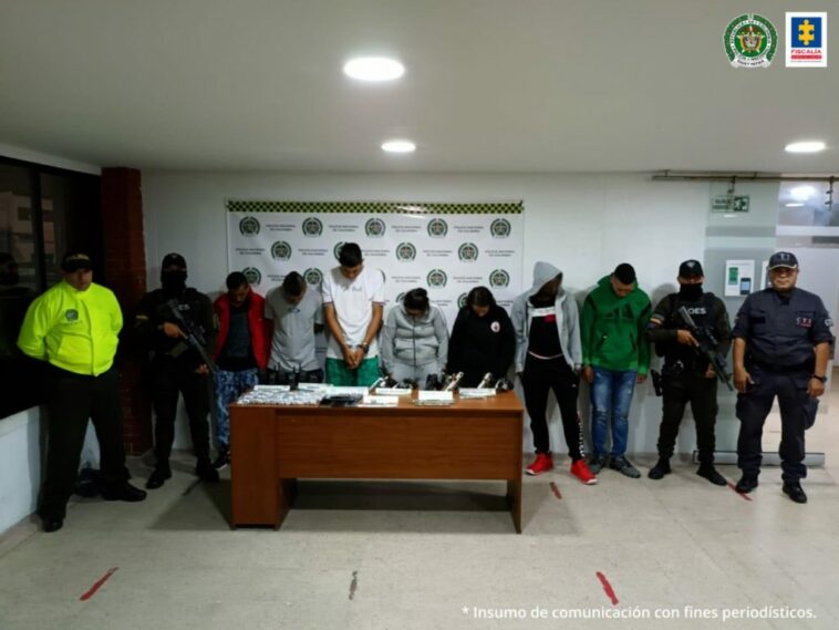 Se observan en fila site capturados. Al lado derecho un funcionario GOES y un funcionario CTI. Al lado izquierdo un funcionario GOES un funcionario Policía Nacional.  Al fondo un pendón de Policía Nacional.  Al frente una mesa con el material incautado en los allanamientos.