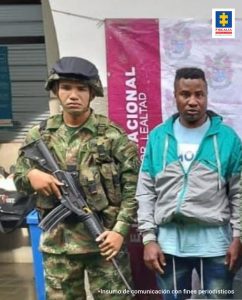 En la foto aparece José Helio Cortés Mesa, alias ‘Dylan’, vestido con chaqueta verde con gris y jean azul. Al lado derecho de él hay un uniformado del Ejército Nacional. Detrás de ellos se aprecia parte de un pendón institucional del Ejército.