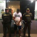 En la fotografía se observa a un hombre con camiseta blanca, bermuda azul, sandalias blancas custodiados por dos agentes de la Policía Nacional en un CAI de Cartagena.