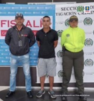 En la fotografía aparece el capturado junto a un investigador del CTI y una uniformada de la Policía Nacional.  En la parte posterior se observan los banners que identifican a la Fiscalía General de la Nación y a la Policía Nacional