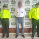 En la imagen el investigado esta de frente, esposado con las manos atrás y custodiado por dos uniformados de la Policía Nacional.