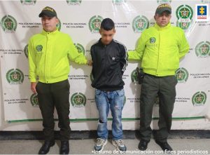 En la fotografía aparece un capturado, junto a personal de Policía Nacional y Fiscalía General de La Nación. En la parte posterior de la imagen se ven banners de Policía Nacional y la Fiscalía General de la Nación.