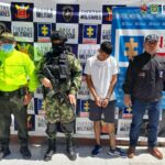 En la fotografía aparece un capturado, junto a personal de Fiscalía General de la Nación, Ejército Nacional y Policía Nacional. En la parte posterior de la imagen se ven banners de Ejército Nacional, Policía Nacional y la Fiscalía General de la Nación.