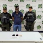 En la foto aparece Leovigildo Mosquera Palacios, alias El Loco o El Compa, con dos funcionarios del Gaula de la Policía Nacional a los lados. Atrás un backing con los logos y adelante una mesa con dos celulares y dos documentos de identificación a los lados.