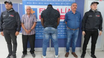 En la imagen se ven tres personas detenidas bajo custodia del CTI y de la Policía. Detrás suyo un backing de la Fiscalía General de la Nación.