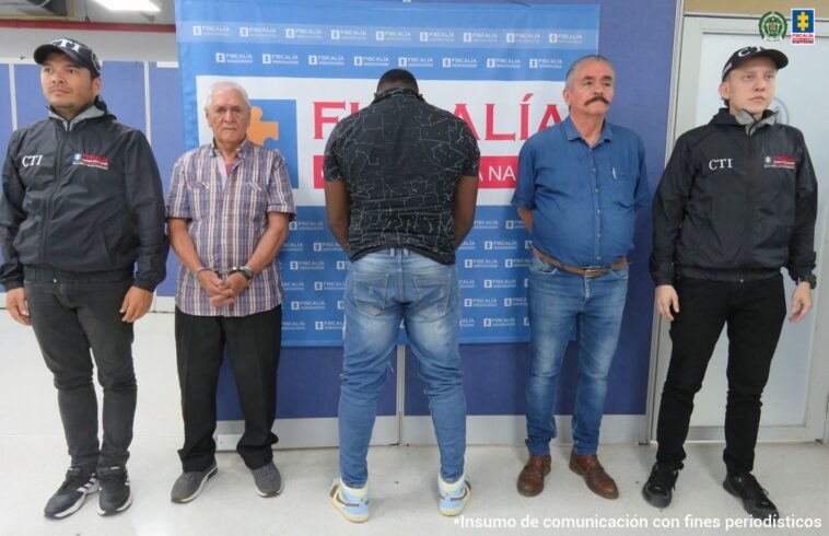 En la imagen se ven tres personas detenidas bajo custodia del CTI y de la Policía. Detrás suyo un backing de la Fiscalía General de la Nación.