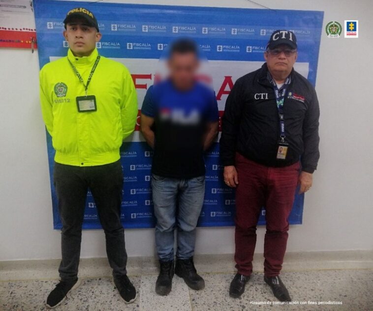 En la fotografía aparece el capturado junto a un investigador del CTI y un uniformado de la Policía Nacional.  Detrás se observa el banner que identifica a la Fiscalía General de la Nación.