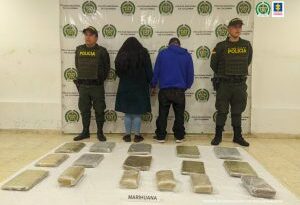 En la fotografía se observa a la pareja capturada junto a dos agentes de la Policía Nacional. En la parte posterior se observan 16 paquetes con marihuana