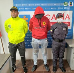 En la foto aparece, de pie Paulo César López Gallego. Viste buzo rojo con capucha y jean azul claro. Al lado derecho de él hay un uniformado de la Policía Nacional. Al lado izquierdo un servidor del CTI de la Fiscalía. Detrás de ellos hay un pendón institucional de la Policía Nacional.