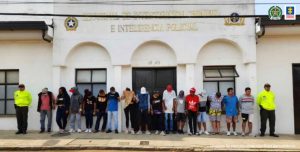 En la imagen se ven 16 personas capturas, frente a un edificio y entre dos policías.