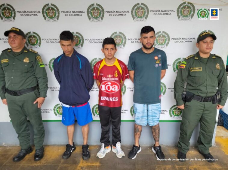 En la imagen se ven tres personas detenidas bajo custodia de dos integrantes de la Policía Nacional. Detrás suyo un backing de la institución.