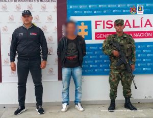 En la fotografía aparece un capturado, junto a personal de Fiscalía General de la Nación y Ejército Nacional. En la parte posterior de la imagen se ven banners de Ejército Nacional y la Fiscalía General de la Nación.