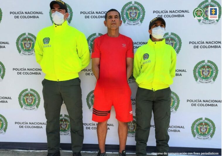 El procesado de camisa roja está esposado y lo acompañan dos uniformados de la Policía Nacional.