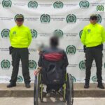 Un hombre aparece de espaldas, sentado en una silla de ruetas. A ambos costados tiene miembros de la Policía.