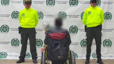 Un hombre aparece de espaldas, sentado en una silla de ruetas. A ambos costados tiene miembros de la Policía.