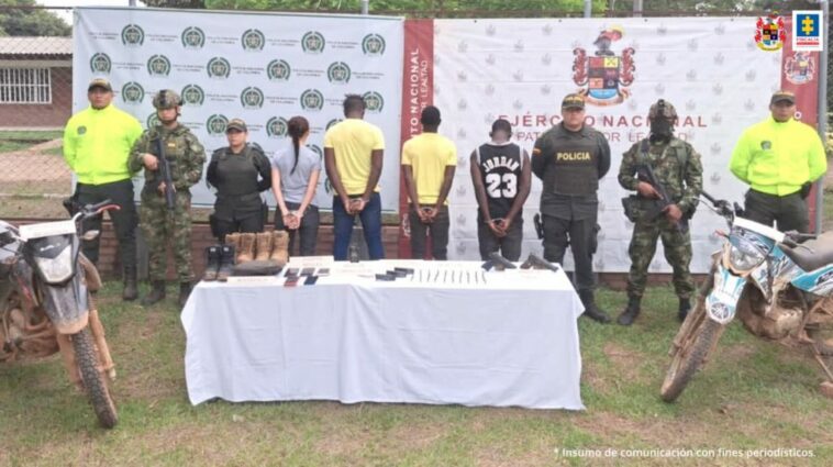 Los capturados están de espalda, y en una mesa aparecen las armas incautadas, equipos celulares y botas, a los costados están dos motocicletas que se les incautó y varios miembros de la Policía y el Ejército Nacional.