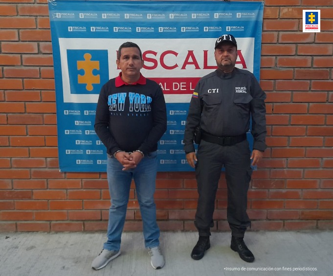 En la fotografía aparece un capturado junto a personal de Fiscalía General de la Nación. En la parte posterior de la imagen se ve un banner de la Fiscalía General de la Nación.