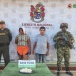 capturado esposado, custodiado por un militar y un policía uniformado, frente a ellos sobre una mesa incautada de droga y detrás de una pancarta del Ejército Nacional