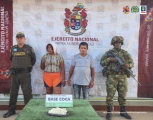 capturado esposado, custodiado por un militar y un policía uniformado, frente a ellos sobre una mesa incautada de droga y detrás de una pancarta del Ejército Nacional