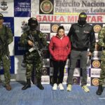 Capturada de frente manos en los bolsillos, custodiada por investigador del CTI de la Fiscalía y soldados del Ejército Nacional. Detrás banner del Gaula Ariari del Ejército Nacional y de la Armada Nacional.