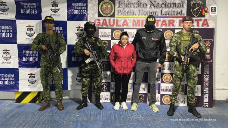 Capturada de frente manos en los bolsillos, custodiada por investigador del CTI de la Fiscalía y soldados del Ejército Nacional. Detrás banner del Gaula Ariari del Ejército Nacional y de la Armada Nacional.