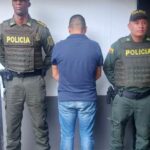 En la fotografía aparece de espaldas a la cámara y con los brazos adelante Jairo Ubaner Díaz Guerrero. Viste camiseta de manga corta color azul y jean azul. Al lado y lado de él hay uniformados de la Policía Nacional.